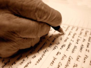 An aged hand uses a pen to write a journal entry in a lined notebook