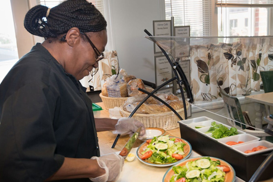 A chef prepares a nutritious salad meal at the counterspace of a dining room.
