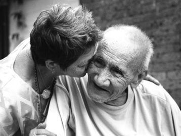A woman kisses an elderly man on the cheek