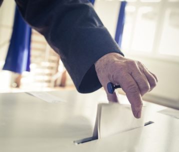 A hand drops a folded paper into a ballot box