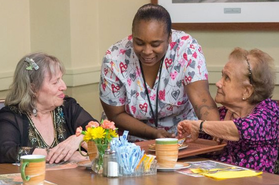 Two women talk with a care provider in the dining area