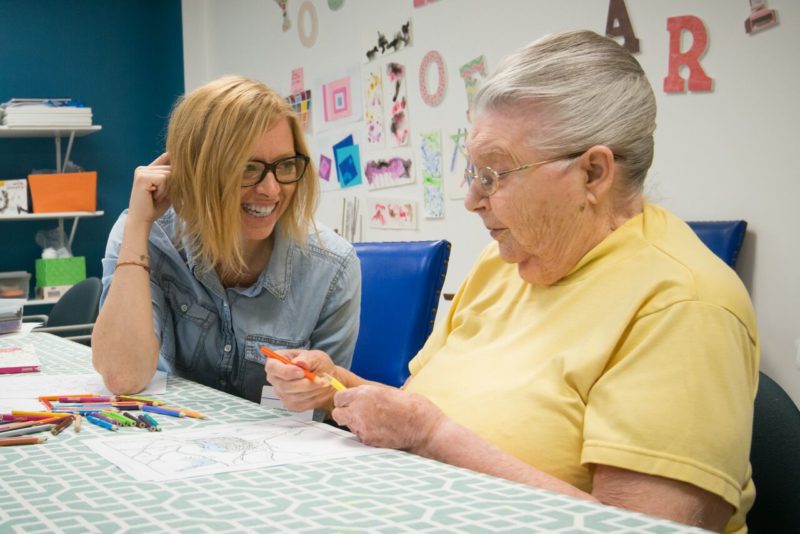 an older woman and a CMSS staff member work on an art project, a common form of memory loss therapy