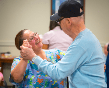 A resident and staff member at a nonprofit senior care community dance as part of an event
