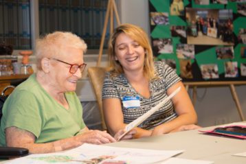 An older woman and a younger woman smile while looking at an art project