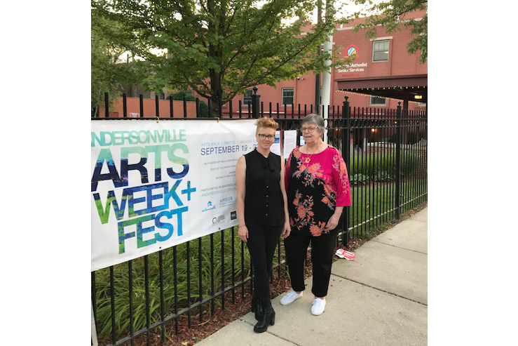 Two people stand outside alongside a banner promoting the Andersonville Arts Week & Fest