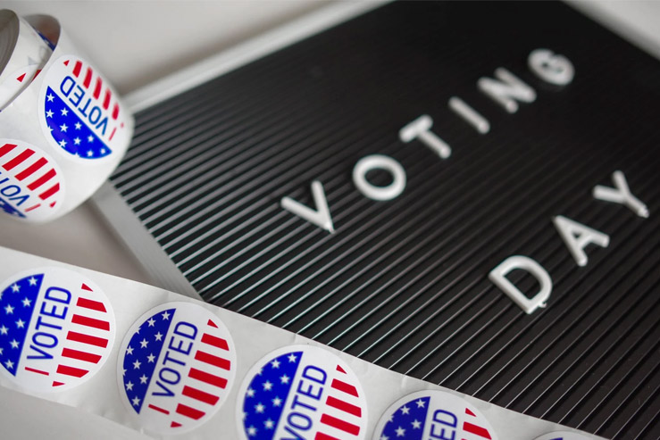 A letterboard with the text: "Voting Day" displayed sits next to a roll of patriotic decorated stickers that contain the text: "I Voted".