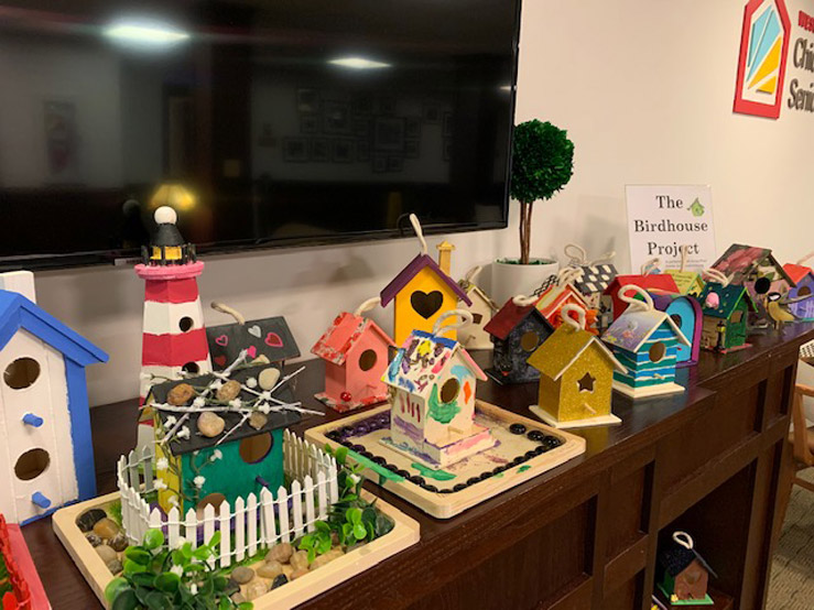 A colorful collection of small hand-painted birdhouses sit on a wooden display shelf.