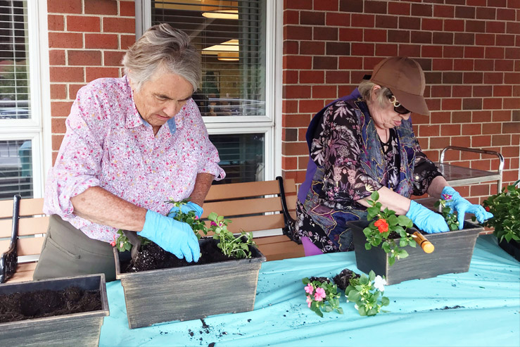 Two women in floral shirts place flowers into new gardening boxes.